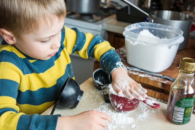Little boy measuring cup of flour, flour all over his hands