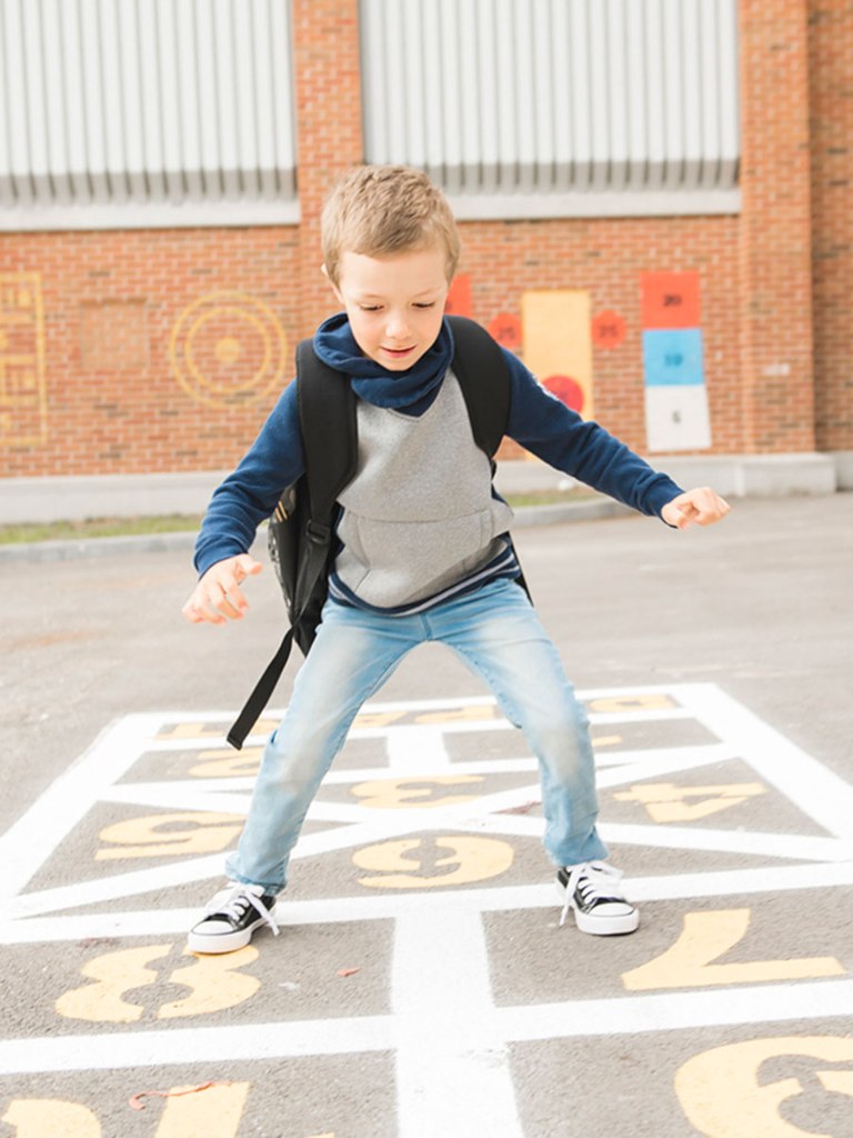 Small blond-haired boy in blue jeans feet apart on the 7-8 of the hopscotch grid